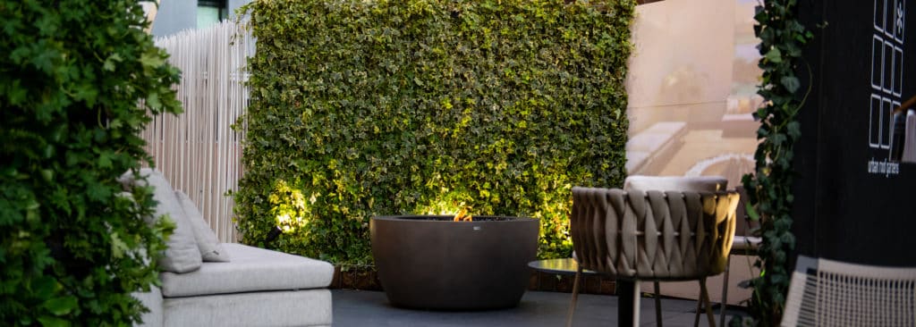 Ivy hedge on a terrace with a lounge sofa, fire bowl and garden chair in evening light