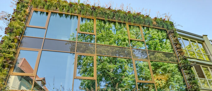 Panorama van een glazen gevel met een groene wand als omlijsting en weerspiegelde bomen